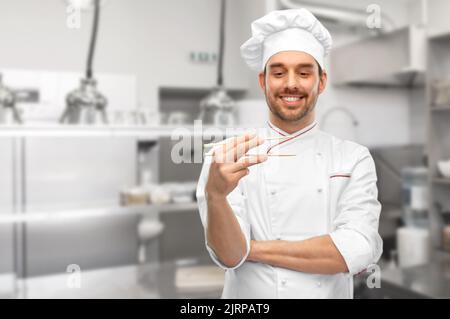 Glücklicher männlicher Koch mit Essstäbchen in der Küche Stockfoto