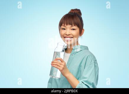 Glückliche asiatische Frau hält Glasflasche mit Wasser Stockfoto