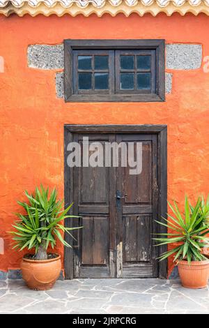 Blick auf ein orangefarbenes Haus mit Holztür und Pflanzen Stockfoto