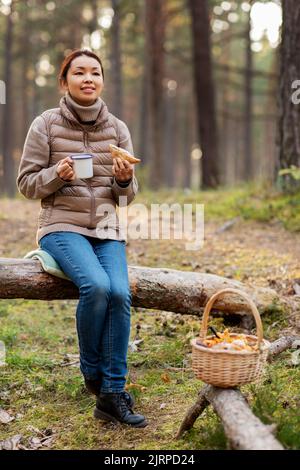 Frau mit Pilzen trinkt Tee und isst im Wald Stockfoto