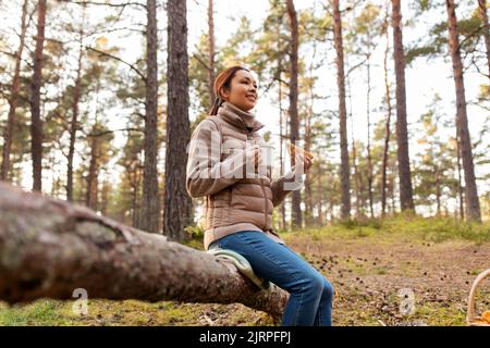 Frau mit Pilzen trinkt Tee und isst im Wald Stockfoto