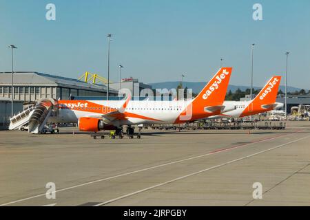 Airbus A320-Flugzeuge mit den Nummern HB–AYP (links) und HB–JZR, die von Easyjet mit Passagiertreppen für die ein- und Ausschiffung von Passagieren auf dem Vorfeld des Genfer Flughafens (GVA) Schweiz unter sonnenblauem Himmel betrieben werden. (131) Stockfoto