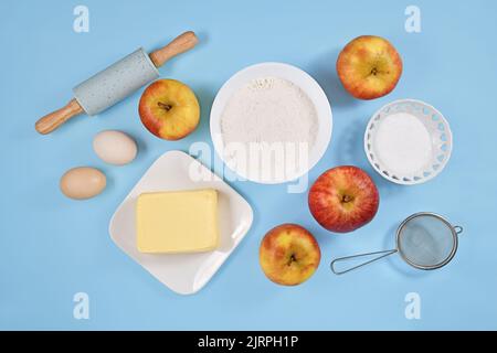 Backzutaten für Apfelkuchen mit Butter, Mehl, Zucker, Eiern und Früchten auf blauem Hintergrund Stockfoto