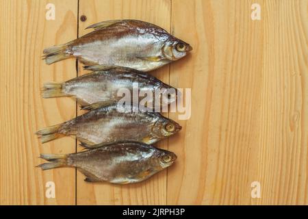 Getrockneter geräucherter Fisch, auf einem leichten Holzbrett, Ansicht von oben. Vier getrocknete Fische auf einem hölzernen Hintergrund. Stockfoto