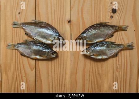 Getrockneter geräucherter Fisch, auf einem leichten Holzbrett, Ansicht von oben. Vier getrocknete Fische auf einem hölzernen Hintergrund. Stockfoto