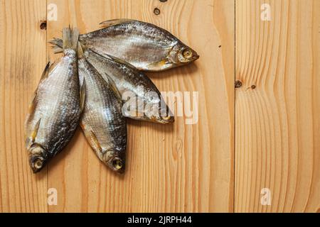 Getrockneter geräucherter Fisch, auf einem leichten Holzbrett, Ansicht von oben. Vier getrocknete Fische auf einem hölzernen Hintergrund. Stockfoto