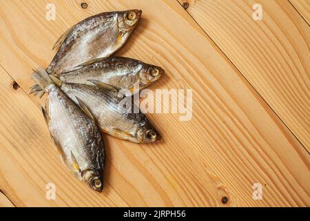 Getrockneter geräucherter Fisch, auf einem leichten Holzbrett, Ansicht von oben. Vier getrocknete Fische auf einem hölzernen Hintergrund. Stockfoto