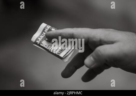 Eine Graustufenaufnahme eines Mannes, der eine Packung gefalteter US-Dollar-Banknoten in den Händen hält Stockfoto