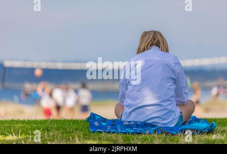 Entspannen Sie Frau genießen Sonne im Park. Junge Frau, die während des Picknicks im Park auf grünem Gras auf Bettzeug mit dem Smartphone sitzt. Mädchen auf dem Gras entspannen. Stockfoto