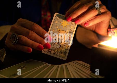 Wahrsagerin weibliche Hände zeigen die Stern Tarot Karte, Symbol der Hoffnung, während einer Lesung. Nahaufnahme bei Kerzenschein, stimmungsvolle Atmosphäre. Stockfoto