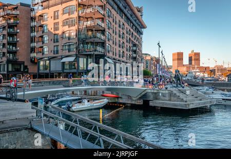 Blick auf die Uferpromenade von Aker Brygge an einem sonnigen Nachmittag im Sommer, mit dem ikonischen Rathaus von Oslo im Hintergrund. Oslo, Norwegen. Stockfoto