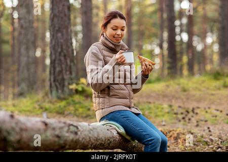 Frau trinkt Tee und isst Sandwich im Wald Stockfoto