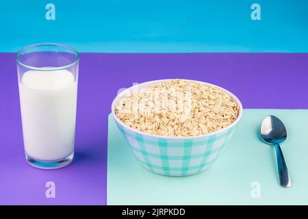 Blick auf einen Teller mit natürlichem Haferflocken mit Bananen und ein Glas frischer Milch vor einem Hintergrund von Pastellfarben, bereit zum Frühstück. Stockfoto