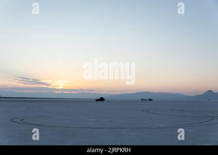 Auto auf den Bonneville Salt Flats in Utah bei Sonnenuntergang mit Reifenpfaden Stockfoto