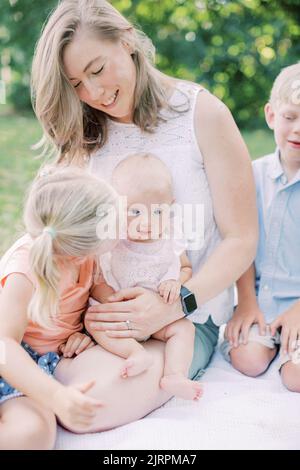 Kleinkind Mädchen küsst Baby Schwester auf Wange, während sie mit der Familie sitzt. Stockfoto