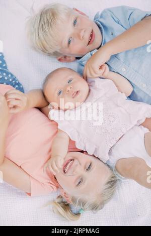 Drei junge, blonde Geschwister lagen auf einer Decke und lächelten vor der Kamera Stockfoto