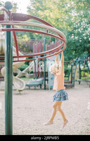 Vier Jahre altes blondes Mädchen hängt von Spielplatzgeräten in Maryland Stockfoto