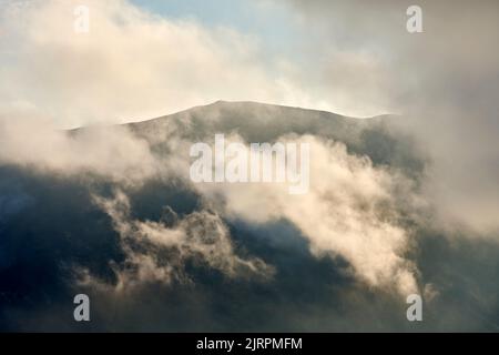Weiße Wolken schweben über vulkanischem bergigen Gelände Stockfoto