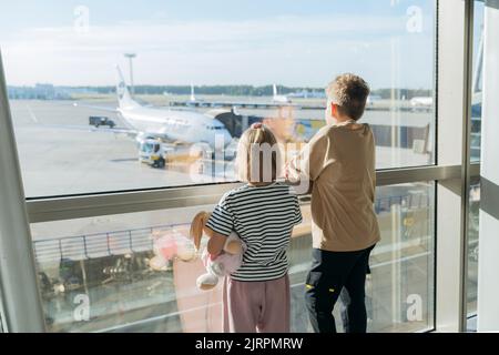 Kinder am Flughafen mit Blick aus dem Fenster auf das Flugzeug. Stockfoto