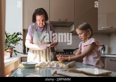 Ur-Großmutter und ihre Enkelin kochen Kuchen in der Küche. Stockfoto