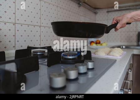 Eine Nahaufnahme einer Bratpfanne wird auf einen Gasherd mit brennendem Gas gestellt. Stockfoto