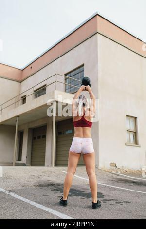 Junge blonde Frau tut Kettlebell Schaukel vor alten Feuer s Stockfoto