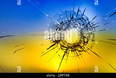 Einschussloch, Risse im Glas auf gelb-blauem Hintergrund. Konzept, Russisch Ukrainischer Krieg. Stockfoto