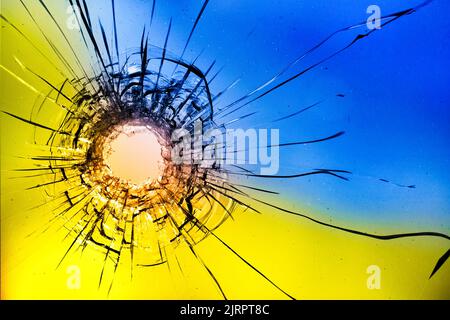 Einschussloch, Risse im Glas auf gelb-blauem Hintergrund. Konzept, Russisch Ukrainischer Krieg. Stockfoto