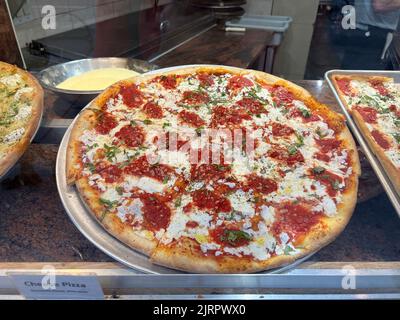 Frisch zubereitete Pizza, die in einer Pizzeria in Manhattan, New York City, am Fenster ausgestellt wird. Stockfoto
