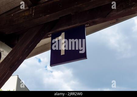 Bahnsteig 1 Schild an einem Bahnhof. Weiße Nummer eins auf einer blauen Metallplatte. Informationen über die an- und Abreise der Züge. Stockfoto