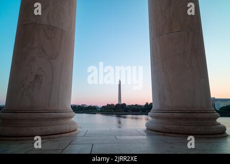 Das Washington Monument und das Weiße Haus sind von der anderen Seite des Tidal Basin aus zu sehen, eingerahmt von zwei Säulen im Jefferson Memorial. Sonnenaufgang im Sommer. Stockfoto