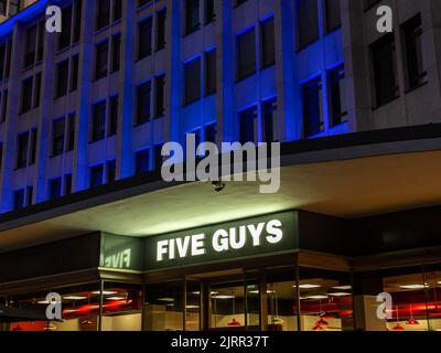 Fünf Jungs Fast-Food-Restaurant am Abend. Beleuchtetes Logo an der Außenfassade eines Gebäudes. Das Zeichen des amerikanischen Geschäfts leuchtet durch das Licht. Stockfoto