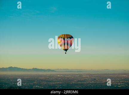 Ein Heißluftballon schwebt gegen den klaren Morgenhimmel über einer von Nebel umhüllten Berglandschaft Stockfoto