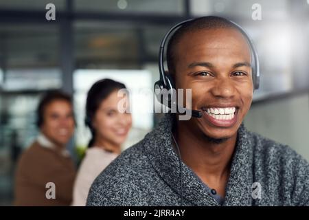 Waren im Standby-Modus, um Ihren Anruf entgegennehmen zu können. Porträt eines Call Center-Agenten, der in einem Büro arbeitet, mit seinen Kollegen im Hintergrund. Stockfoto