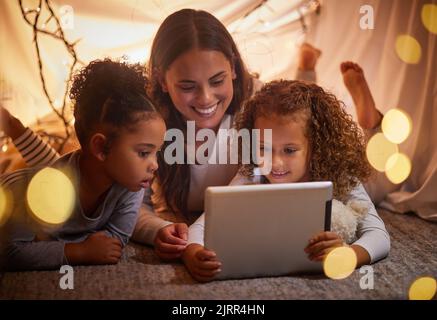 Heimzelt Mutter und Kinder auf dem Tablet sehen sich abends im Haus Filme oder Online-Unterhaltungsfilme für Kinder an. Glückliches Lächeln Mutter oder Frau und junges Mädchen Stockfoto