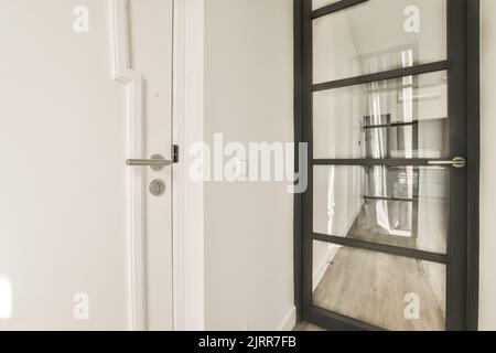 Komfortables Bett mit Federdecke und Kissen in der Nähe von Stuhl und Wand mit gerahmten Gemälden am Kleiderschrank im beleuchteten Schlafzimmer Stockfoto