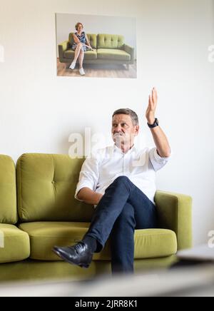 Mainz, Deutschland. 24. August 2022. Christian Baldauf, CDU-Landesvorsitzender und Fraktionschef seiner Partei im landtag Rheinland-Pfalz, sitzt in der Redaktion unter einem Foto von Ministerpräsident Malu Dreyer (SPD) während eines Interviews mit der Deutschen Presse-Agentur (dpa) auf dem Grünen Sofa. (To dpa 'Baldauf: Für Lewentz wird die Luft 'sehr dünn') Quelle: Frank Rumpenhorst/dpa/Alamy Live News Stockfoto