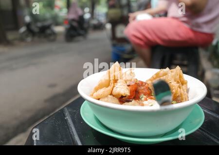 Leckeres indonesisches Street Food Bakwan Malang serviert in einer Schüssel mit sitzender weiblicher Käuferin im Hintergrund Stockfoto