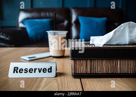 Eine Tasse Eiskaffee auf einem reservierten Tisch im Restaurant mit Ledersofa und blauen Kissen im Hintergrund Stockfoto