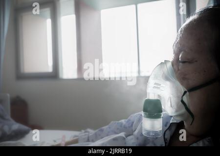 Südostasiatische ältere Patientin hospitalisiert und beatmet mit Vernebler im Krankenhausbett Stockfoto