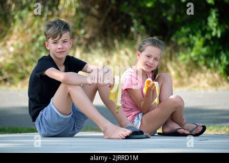 Junge hübsche Teenager Junge und hübsches Mädchen essen leckere reife Banane Naschen im Freien am Sommertag Stockfoto