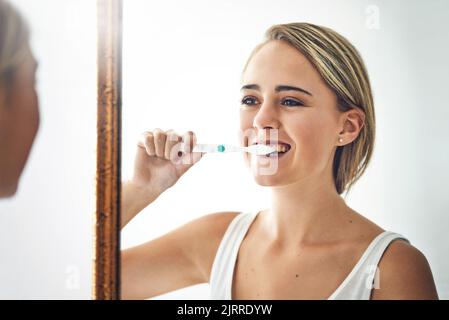 Je gesünder sie sind, desto schöner ist Ihr Lächeln. Porträt einer attraktiven jungen Frau, die sich im Badezimmer die Zähne putzt. Stockfoto