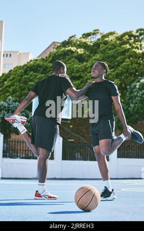 Fit, aktiv und sportlich junge Basketballspieler strecken oder wärmen ihre Beine auf einem Basketballplatz auf. Entschlossene männliche Athleten bereiten Muskelfitness vor Stockfoto