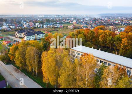 Luftaufnahme des Schul-, College- oder Kindergartengebäudes mit großem Hof unter Herbstbäumen auf dem ländlichen Landschaftshintergrund Stockfoto