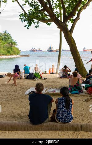 Entspannen Sie sich am Siloso Beach mit Containerschiffen vor Anker, Sentosa Island, Singapur Stockfoto