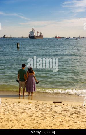 Entspannen Sie sich am Siloso Beach mit Containerschiffen vor Anker, Sentosa Island, Singapur Stockfoto