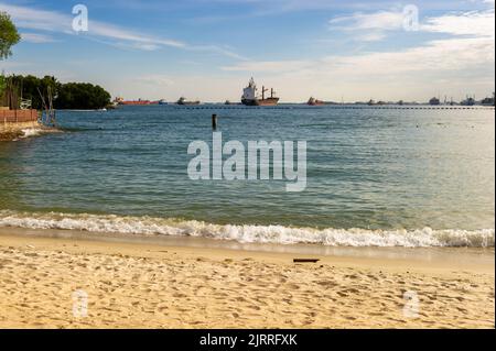 Entspannen Sie sich am Siloso Beach mit Containerschiffen vor Anker, Sentosa Island, Singapur Stockfoto