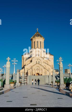 Eine Rückansicht von Menschen, die in Richtung der Kathedrale der Heiligen Dreifaltigkeit von Tiflis auf blauem Himmel gehen Stockfoto