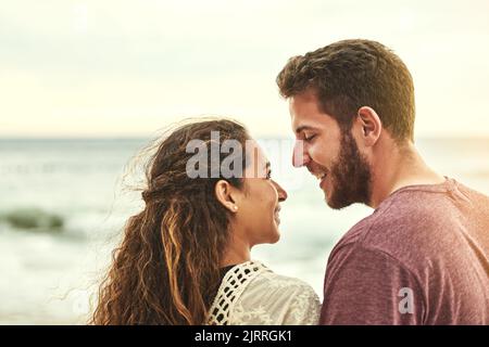 Ich konnte mich in diesen Augen verlaufen. Ein liebevolles junges Paar, das ihre Zeit am Strand genießt. Stockfoto