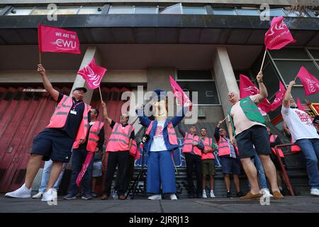 Eine als Kinderbuchfigur gekleidete Person, Postmann Pat, trifft Postarbeiter der Communication Workers Union (CWU) auf die Streikposten am Royal Mail Whitechapel Delivery Office im Osten Londons. Mehr als 100.000 Postarbeiter sollen am Freitag in einem Lohnstreit auslaufen, und zwar in dem, was bisher als größter Streik des Sommers bezeichnet wird. Bilddatum: Freitag, 26. August 2022. Stockfoto